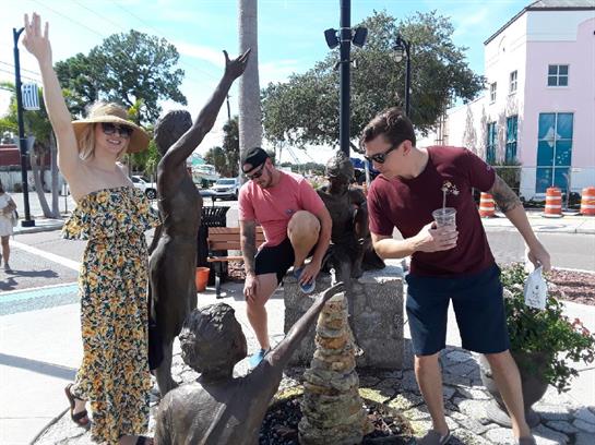 Three friends smiling and posing with a statue on a sunny day, enjoying their time together.