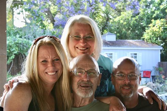 Four friends are smiling and posing together in a lush green backyard adorned with flowers.