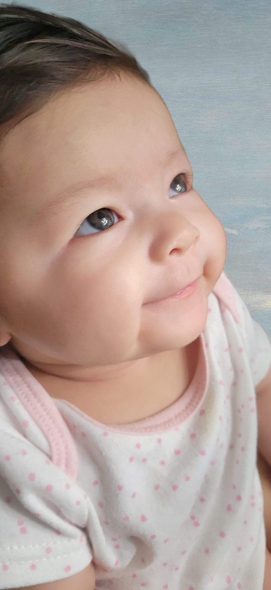 A joyful baby with bright eyes smiles while looking up in a serene indoor space.