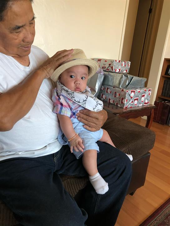 A grandfather lovingly holds his grandchild in a cozy living room filled with gifts.