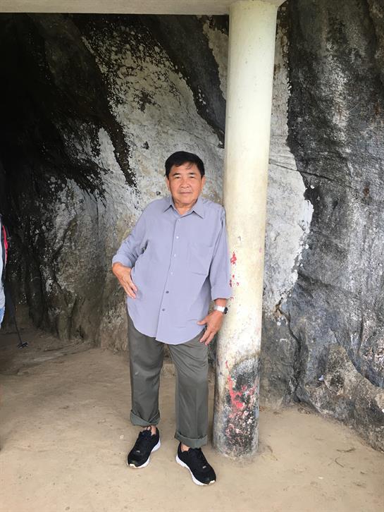 A man poses beside a pillar in a rocky cave, enjoying the outdoors on a sunny day.