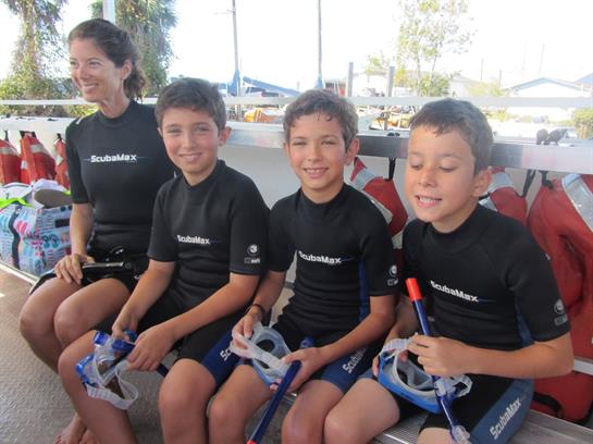 A group of children and an adult prepare for a snorkeling adventure while sitting in the sun.