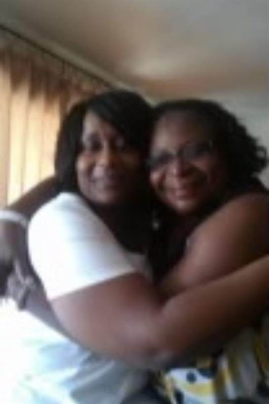 Two women joyfully embrace each other indoors, surrounded by soft lighting and warmth.