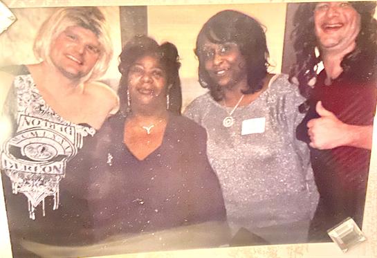 Four women stand closely together, smiling and enjoying a lively gathering in a casual environment.