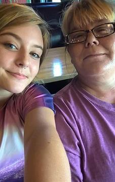 Two women share a joyful selfie, showing their smiles and casual outfits in a bright setting.