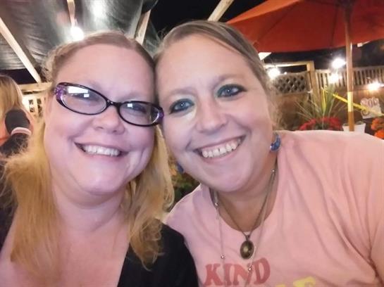 Two smiling women pose together, enjoying a sociable evening under bright lights and umbrellas.