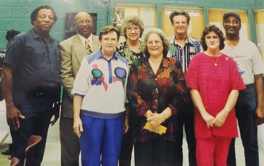 A diverse group of friends poses together, smiling at a community event in the 1990s.