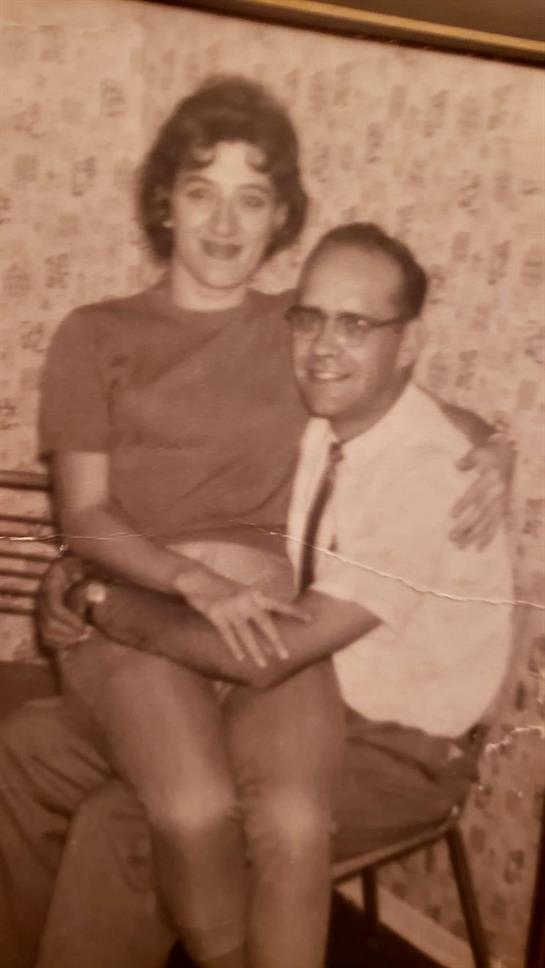A young woman sits on a man's lap, both dressed in casual clothing, exuding joy and affection.