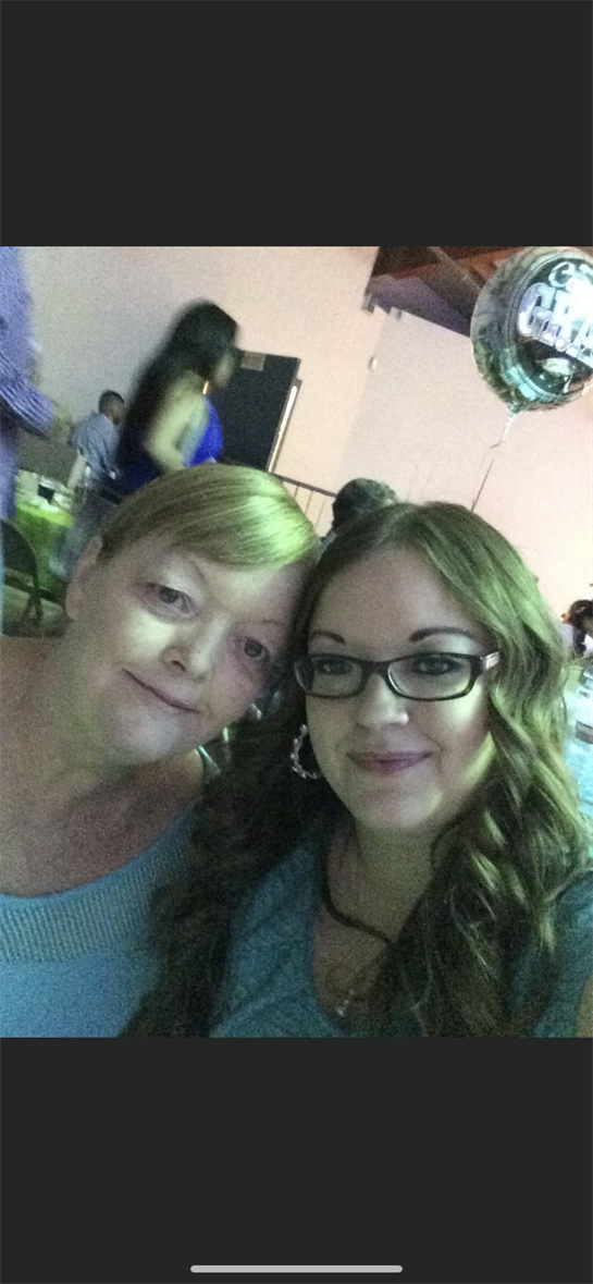 Two women are smiling closely together at a lively gathering filled with friends and celebrations.