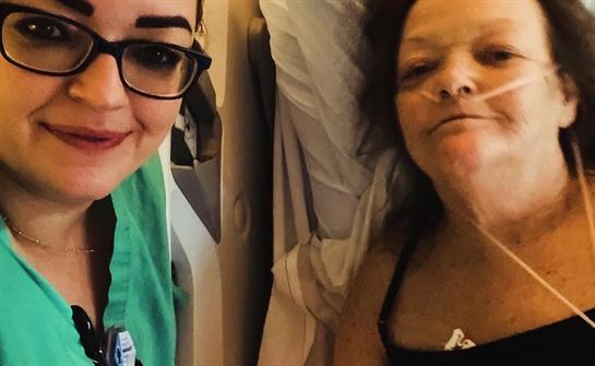 A caregiver smiles alongside a patient resting in a hospital bed, showing a supportive environment.