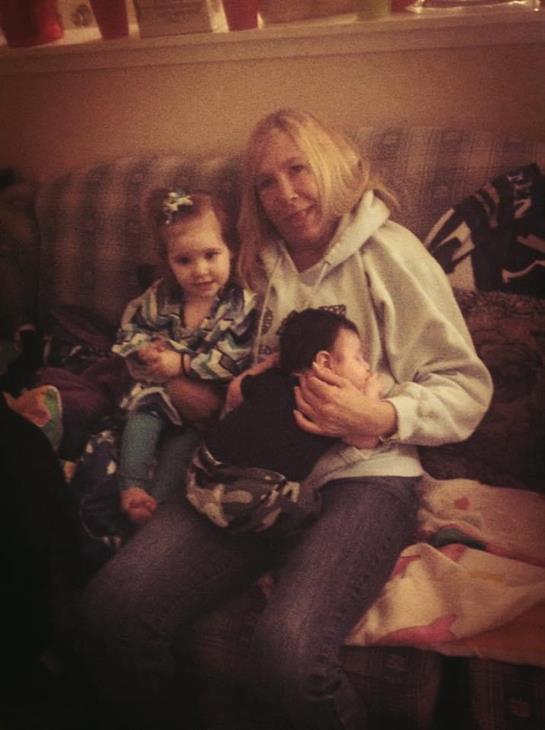 A woman holds a baby and sits beside a young girl in a welcoming living room.