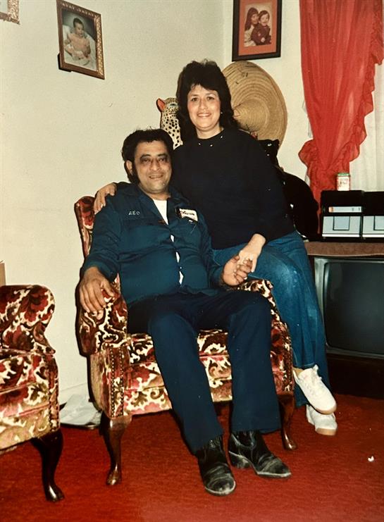 A couple relaxes on a vintage armchair in a charming living room decorated with family photos.
