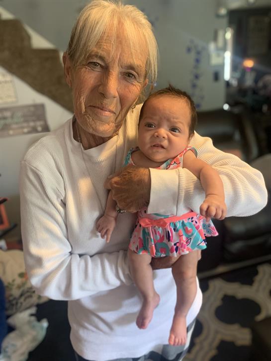 An elderly woman joyfully carries a baby in a casual home setting filled with warmth and love.