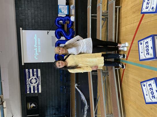 Two students celebrate graduation in a decorated school gym with themed decorations.