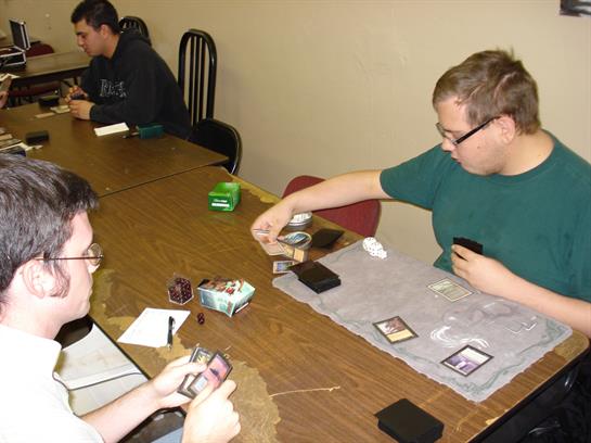 Two friends focus on card strategies while competing in a game at a table with supplies.