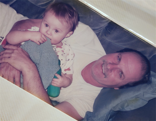 A man relaxes on a couch with a young child, sharing smiles and warmth together.