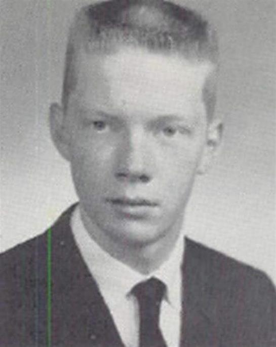 A young man wears a suit and tie, posing for a formal school portrait in the 1960s.