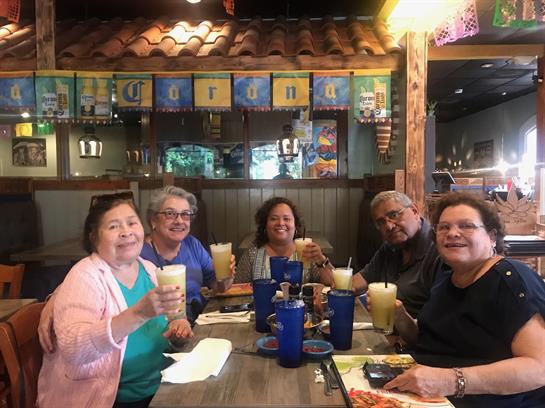 Five friends toast with drinks in a lively restaurant adorned with colorful decorations.