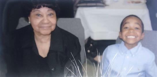 A joyful child grins widely beside his grandmother while celebrating with family.