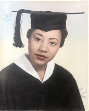 A young woman proudly displays her graduation cap and gown in a posed portrait.