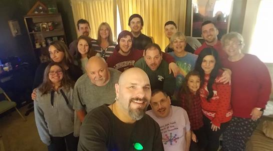A large group of family members poses together, smiling and celebrating in a warm living room.