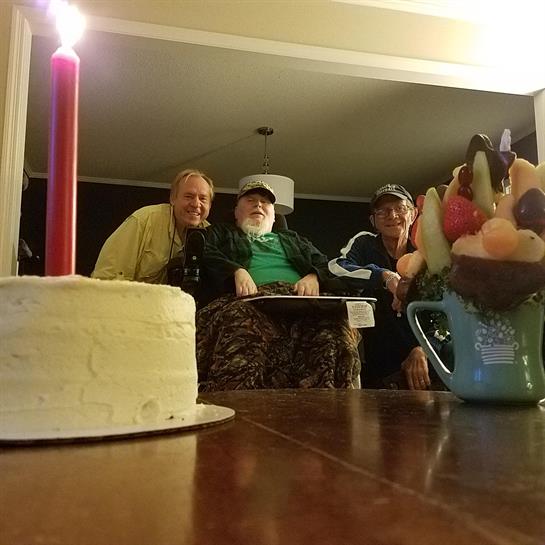 Friends celebrate with a cake and candles in a warm living room environment.