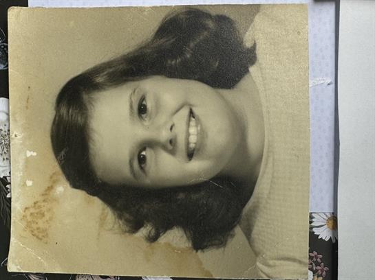 A young girl with curly dark hair smiles happily while posing for a vintage portrait.