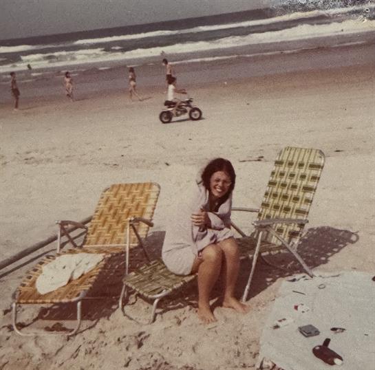 A group relaxes on beach chairs while a woman smiles and holds a drink.