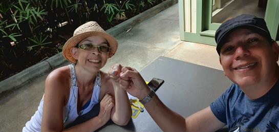 Two people share a playful moment, smiling and using hand gestures outdoors.