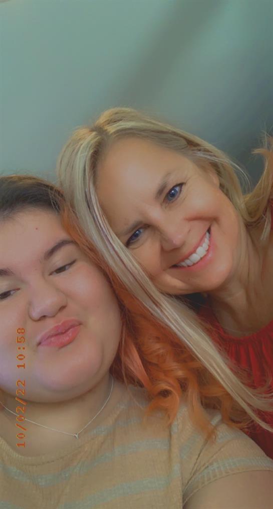 Two women with bright smiles share a close moment while taking a selfie indoors.