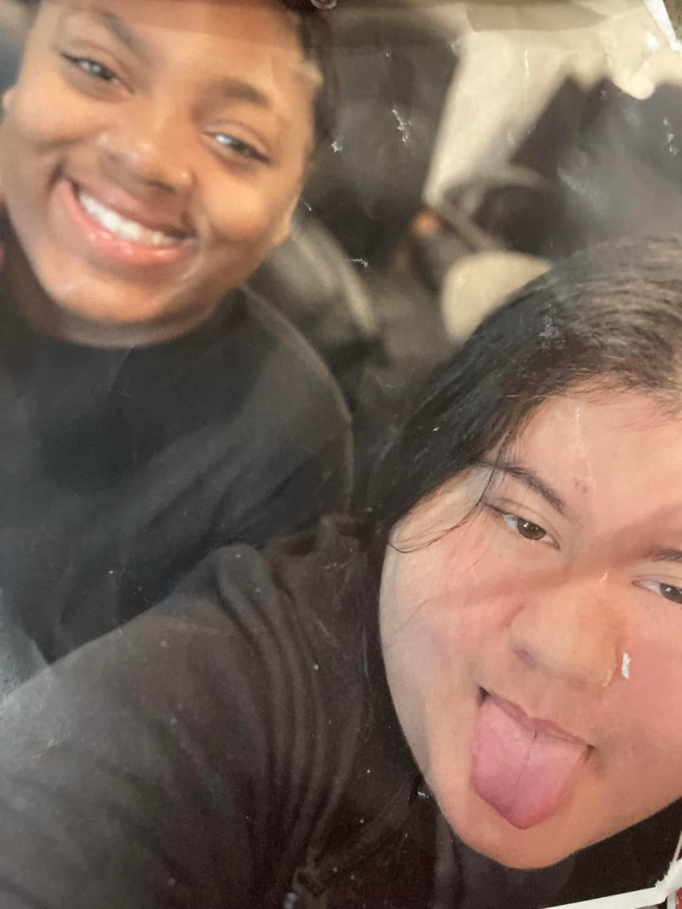 Two friends are smiling and making playful faces while taking a selfie indoors.