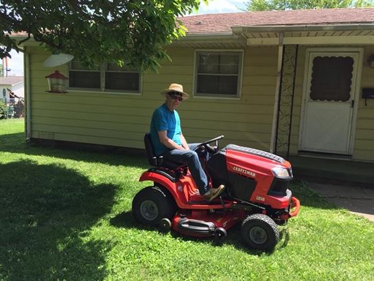 A person enjoys mowing the grass in a vibrant yard on a warm, sunny day.