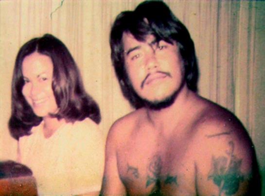 A couple shares a joyful moment together indoors, relaxed and smiling, showcasing the 1970s vibe.