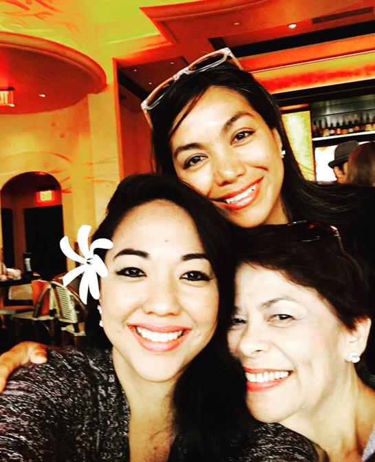 Three women share laughter and smiles while posing together in a lively restaurant atmosphere.
