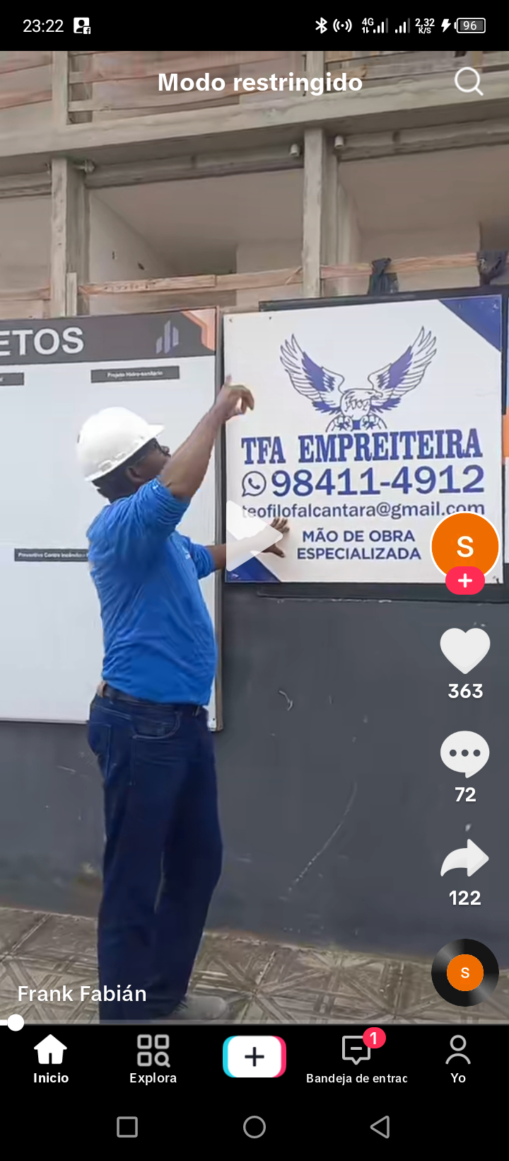 A worker in a blue shirt and helmet is installing a sign for a construction business.