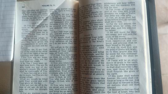 An open book lies on a surface, revealing printed text on yellowed pages in soft lighting.