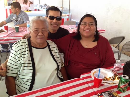 Three family members enjoy a joyful moment together at a lively outdoor gathering filled with food.
