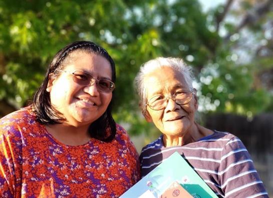 Two women share a joyful moment outdoors, surrounded by greenery and sunlight, smiling happily.