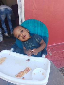 A young child is happily eating snacks in a high chair, displaying a messy tray.