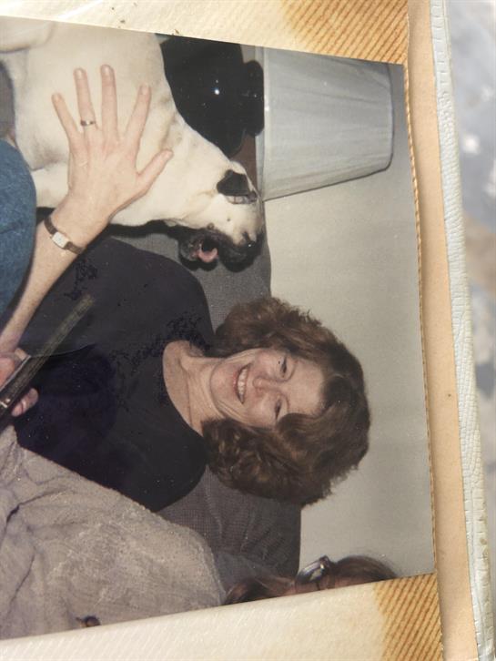 A cheerful woman enjoys her time on the couch while interacting with a playful dog nearby.