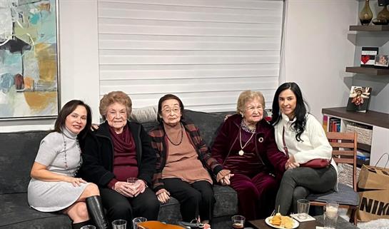 Five women of various ages share stories and laughter on a cozy sofa.