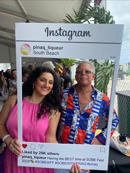 Two friends celebrate at a vibrant South Beach event, sharing smiles with an Instagram frame.