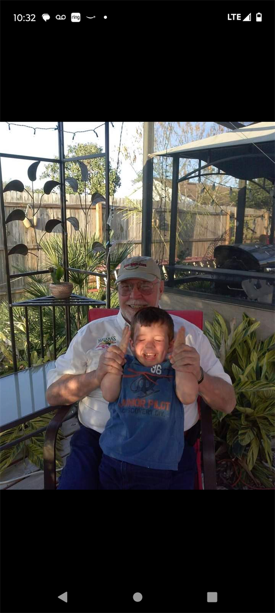 A joyful grandfather sits in a garden chair, holding his laughing grandchild outdoors.