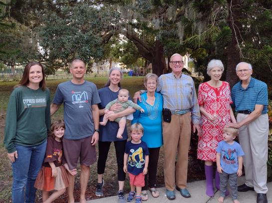 A group of nine people of various ages stands together outdoors, bonding and smiling happily.