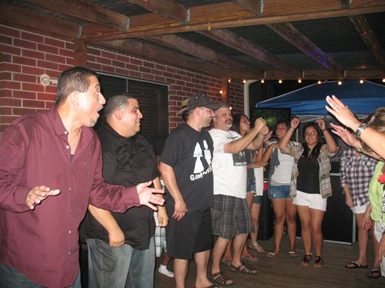 Friends gather for dancing and celebration on a wooden deck under string lights.