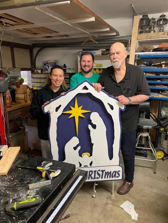 Three individuals work together to create a Christmas nativity scene in a garage.