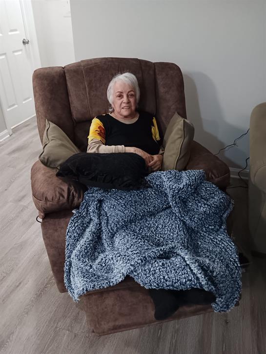 An elderly woman seated comfortably in a chair, enjoying a quiet moment at home.