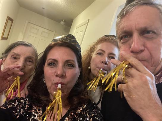 Four friends pose together, wearing party hats and blowing noisemakers in a festive atmosphere.