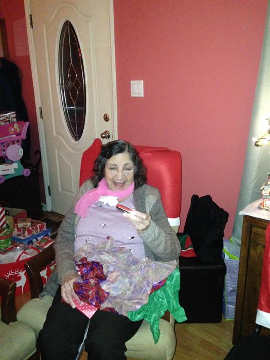 Family gathering takes place as a woman enjoys unwrapping gifts in a cheerful environment.