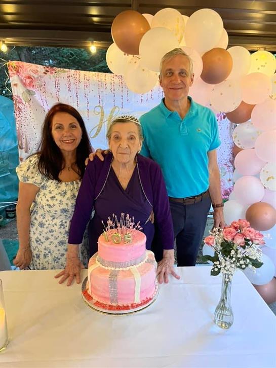 Family members celebrate a birthday with a pink cake and joyful smiles in a decorated venue.